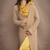a woman wears a long cashmere cardigan coat in sand beige colour over silk top and trousers in butter yellow by Irish brand Madigan