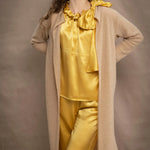 a woman wears a long cashmere cardigan coat in sand beige colour over silk top and trousers in butter yellow by Irish brand Madigan
