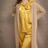 a woman wears a long cashmere cardigan coat in sand beige colour over silk top and trousers in butter yellow by Irish brand Madigan