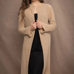 a woman wears a long cashmere cardigan coat in sand beige colour over black linen clothing by Irish brand Madigan