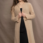 a woman wears a long cashmere cardigan coat in sand beige colour over black linen clothing by Irish brand Madigan