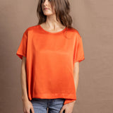 A woman wears an oversized 100% silk t-shirt in orange