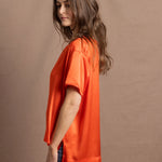 A woman wears an oversized 100% silk t-shirt in orange