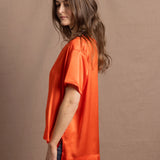 A woman wears an oversized 100% silk t-shirt in orange
