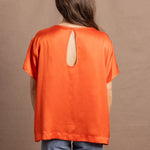 A woman wears an oversized 100% silk t-shirt in orange with a keyhole detail cutout in the back
