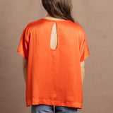 A woman wears an oversized 100% silk t-shirt in orange with a keyhole detail cutout in the back