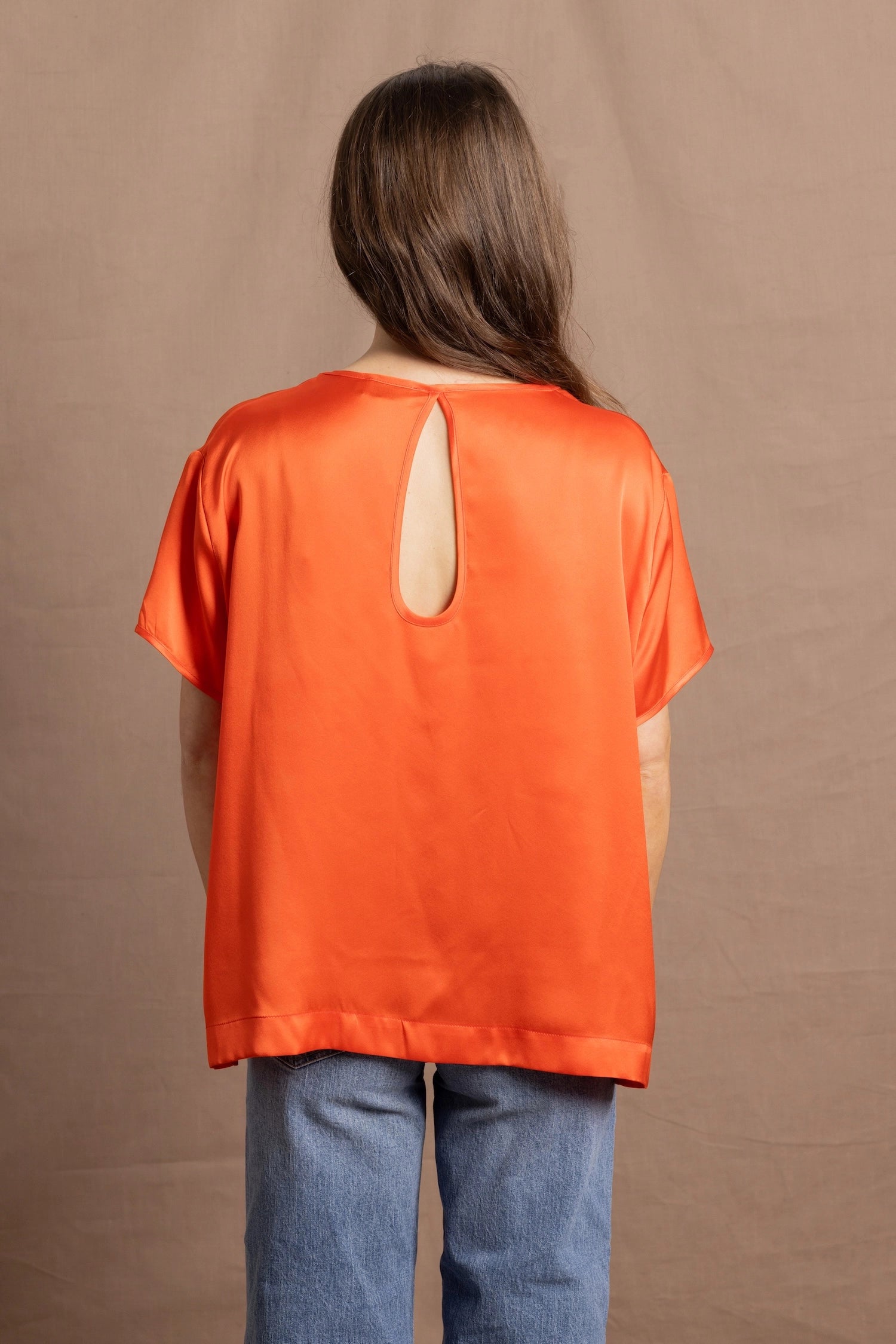 A woman wears an oversized 100% silk t-shirt in orange with a keyhole detail cutout in the back