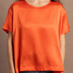 A woman wears an oversized 100% silk t-shirt in orange