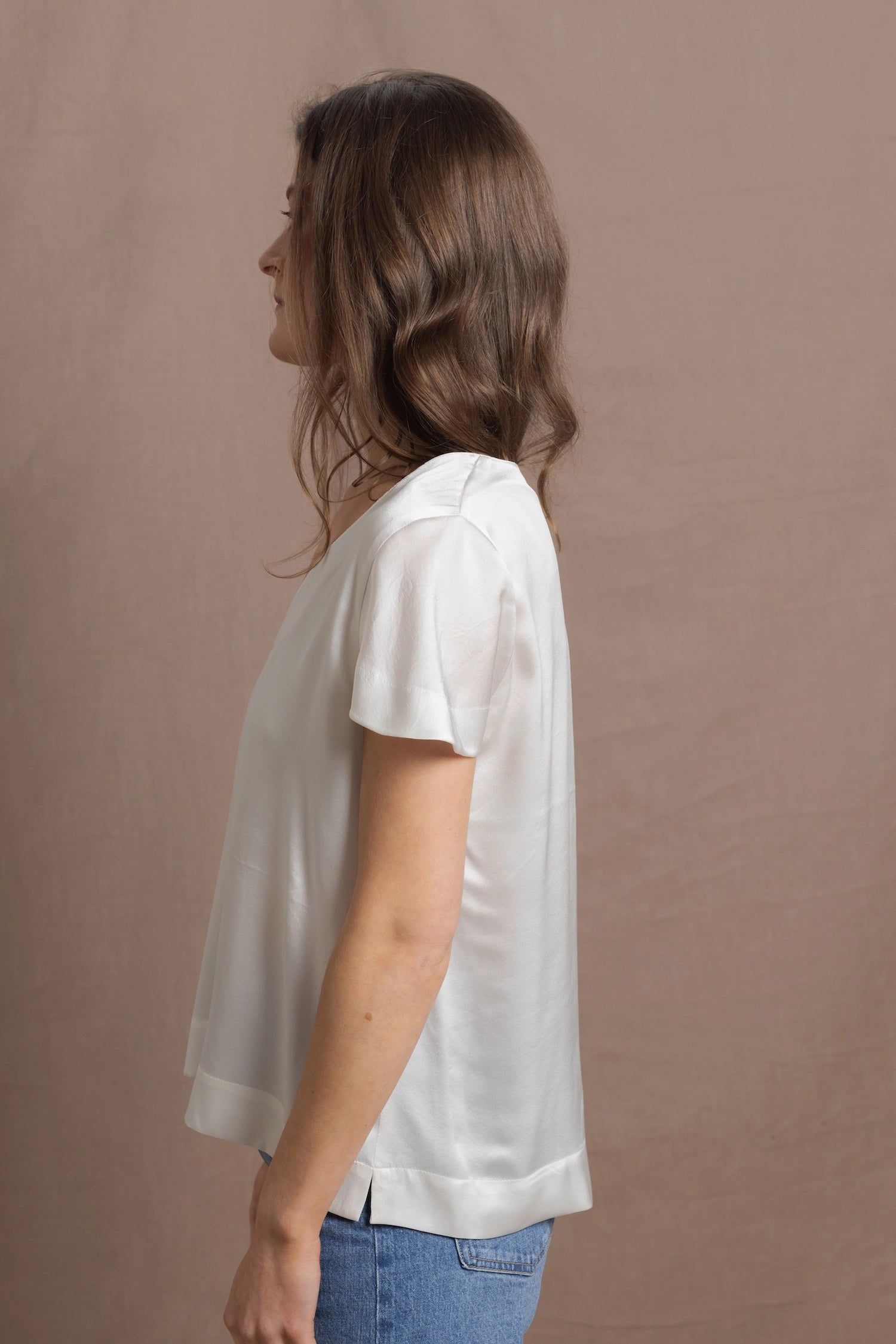 A woman wears a 100% silk v-neck t-shirt in white with a pair of jeans