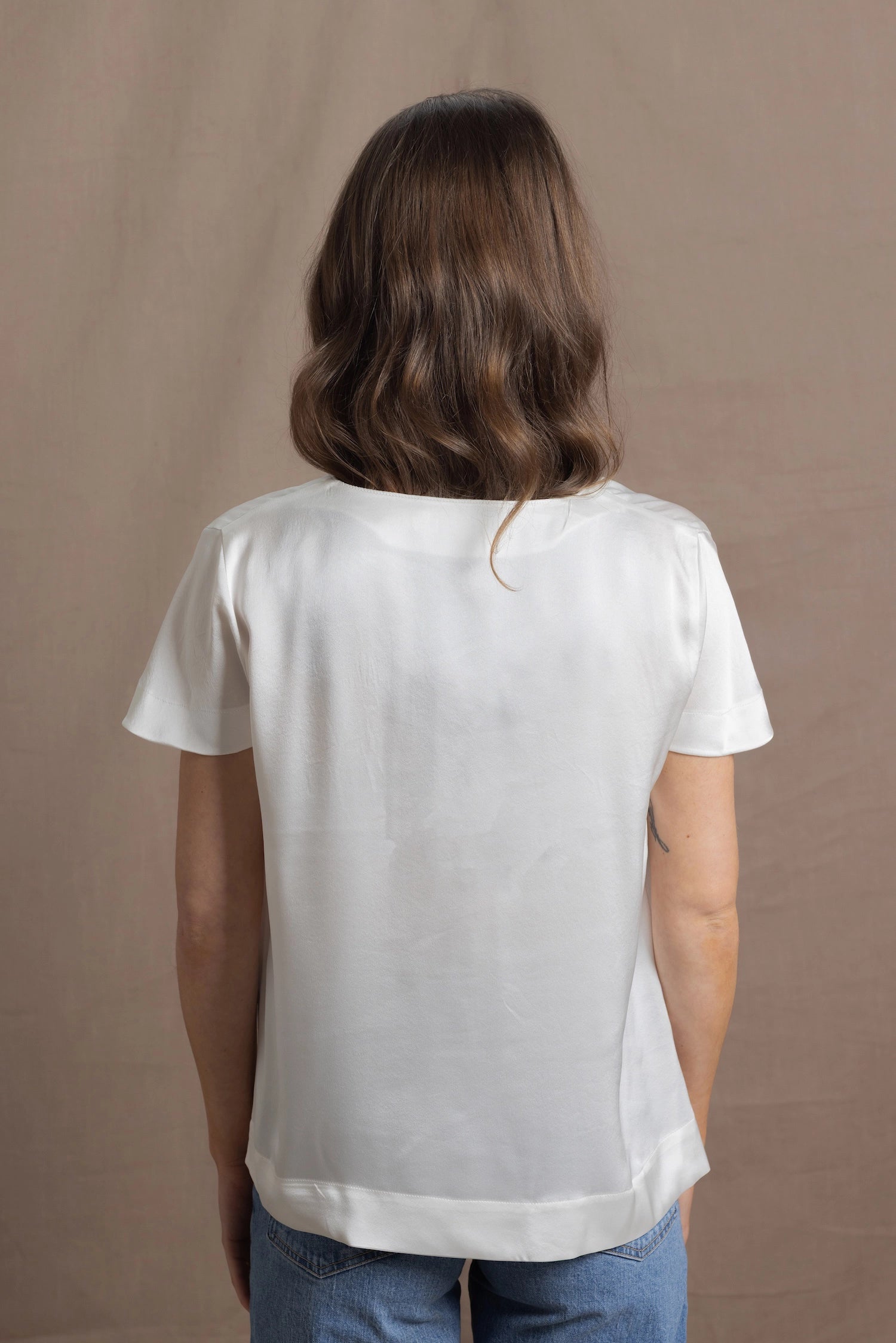 A woman wears a 100% silk v-neck t-shirt in white with a pair of jeans