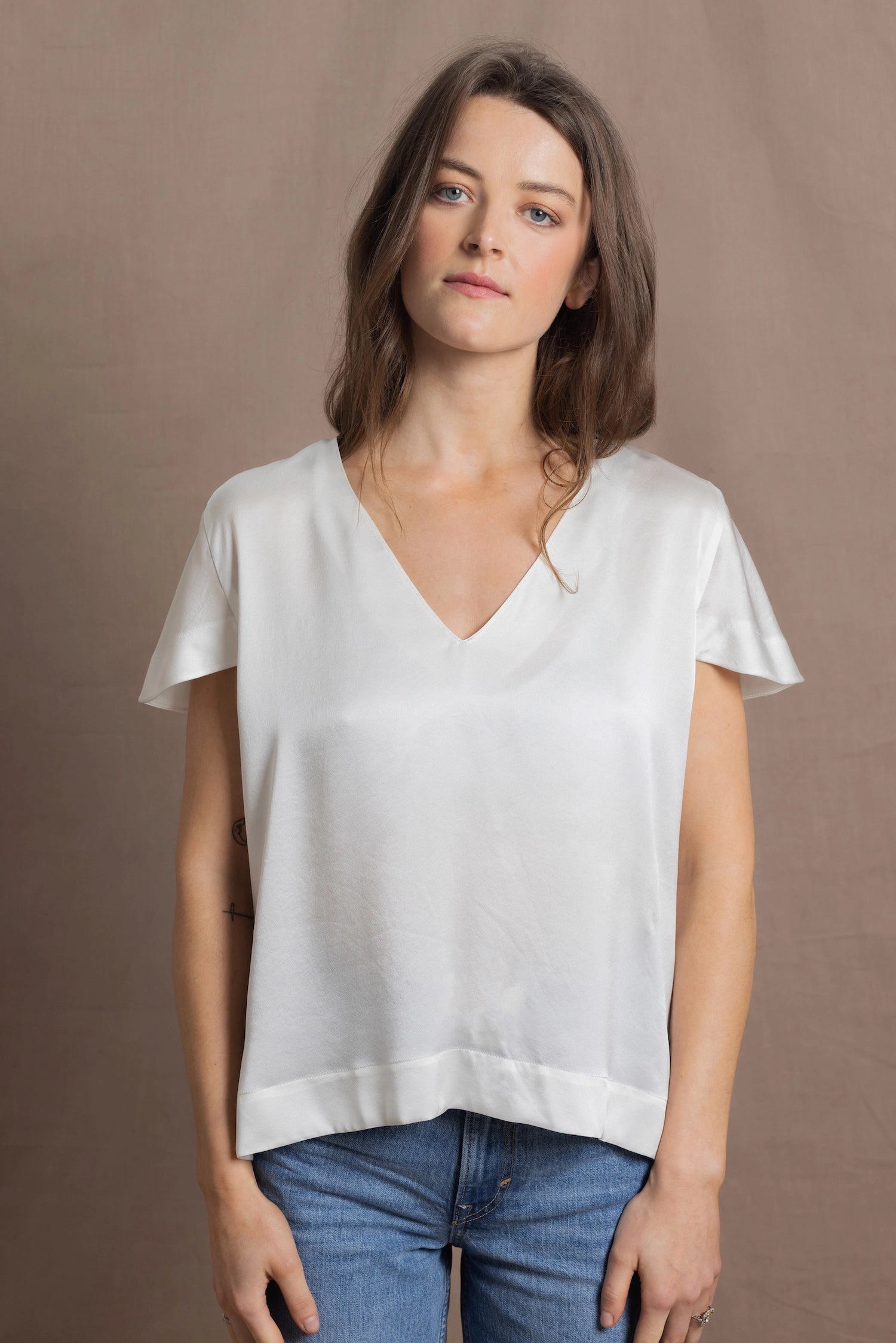 A woman wears a 100% silk v-neck t-shirt in white with a pair of jeans