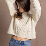 a woman wears a cropped cashmere aran sweater with her hands up in the air and wearing jeans