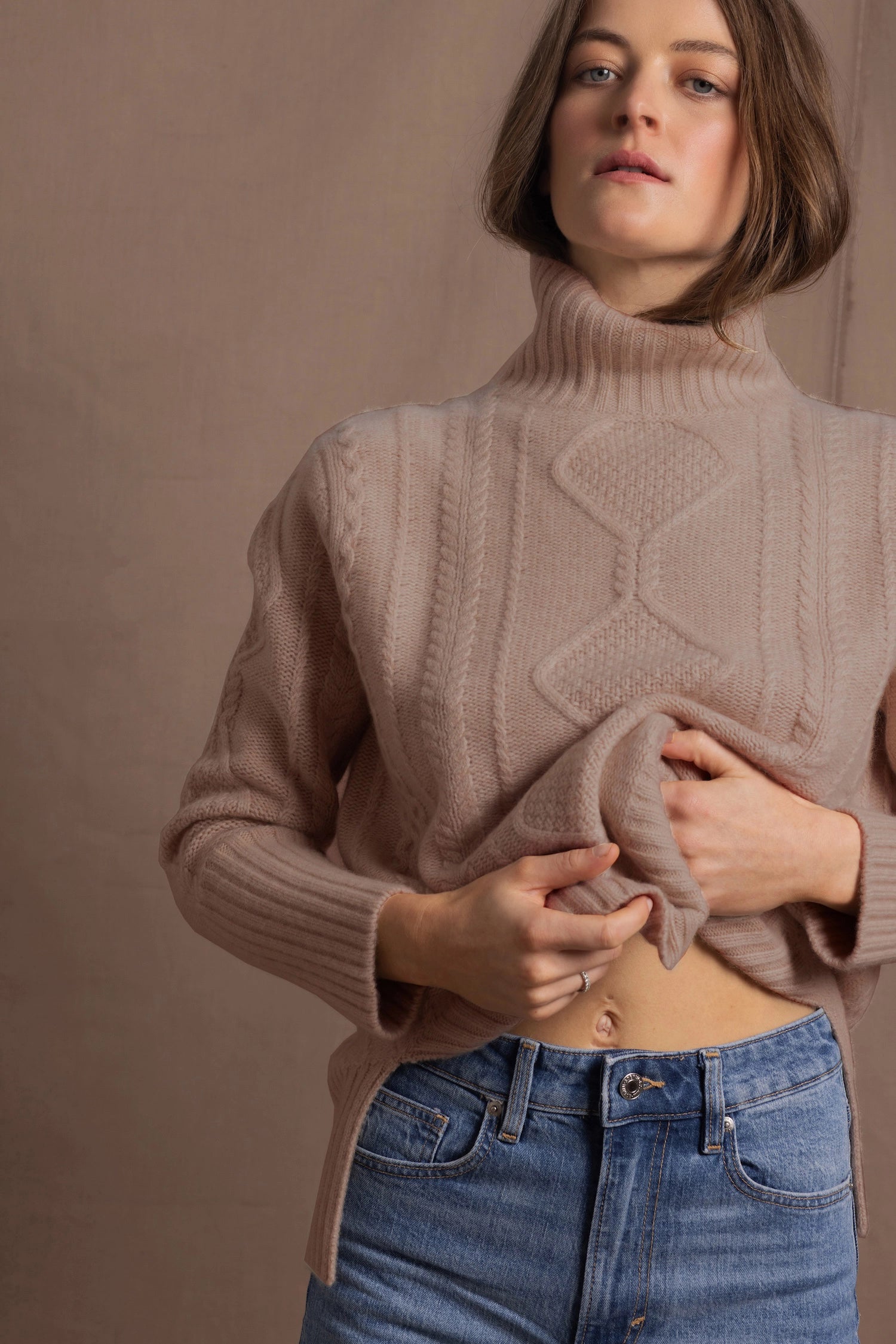 a woman wears a taupe coloured cashmere aran turtleneck sweater