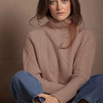 a woman wears a taupe coloured cashmere aran turtleneck sweater