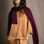 A woman wears a small cashmere scarf in plum burgundy and chocolate brown by Irish brand Madigan Cashmere