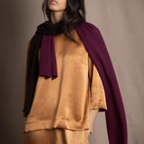 A woman wears a small cashmere scarf in plum burgundy and chocolate brown by Irish brand Madigan Cashmere