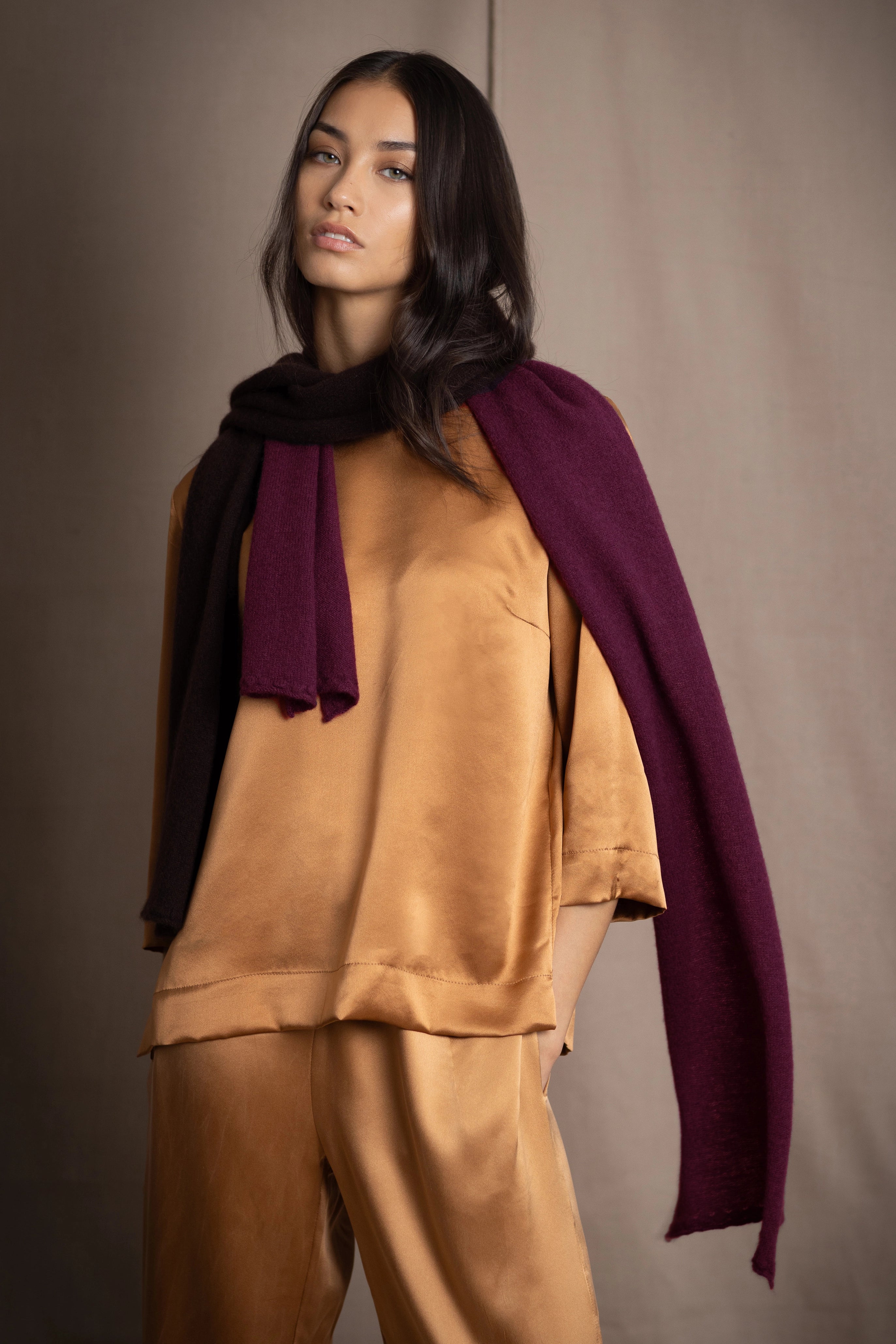 A woman wears a small cashmere scarf in plum burgundy and chocolate brown by Irish brand Madigan Cashmere