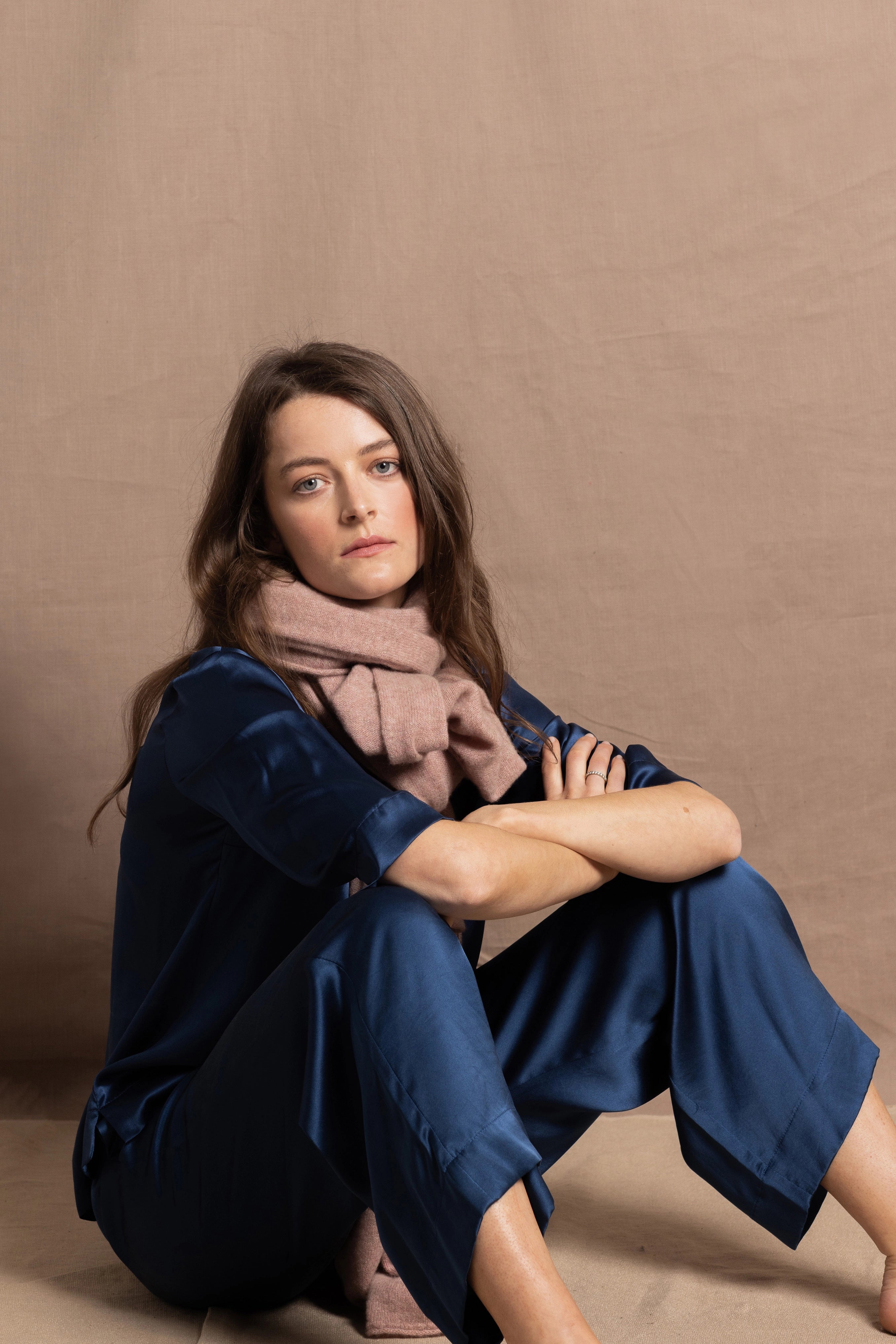 A woman wears a small 100% cashmere scarf in blush pink over a teal 100% silk top and matching trousers