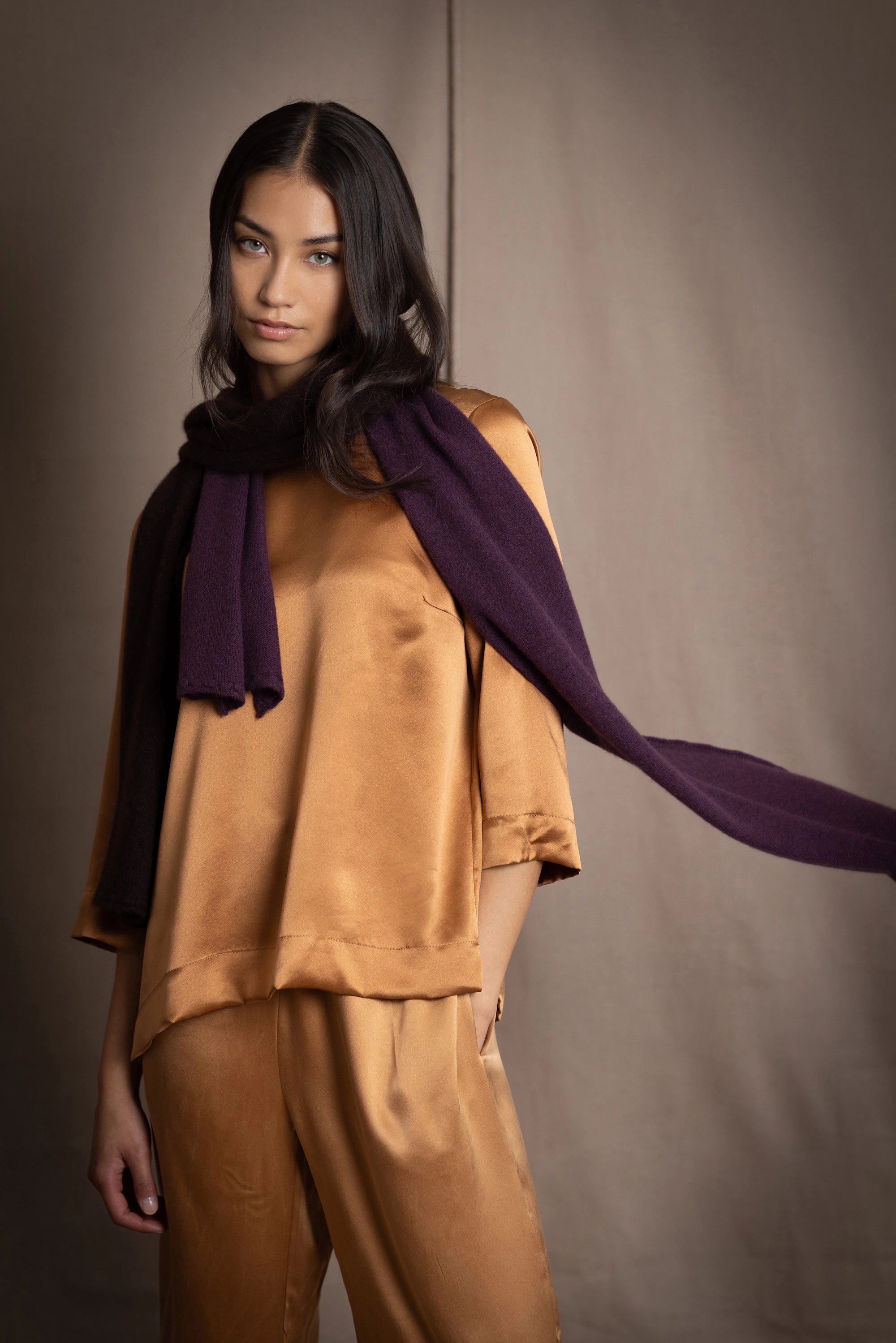 a woman wearing a cashmere scarf in dark purple over bronze silk clothing 