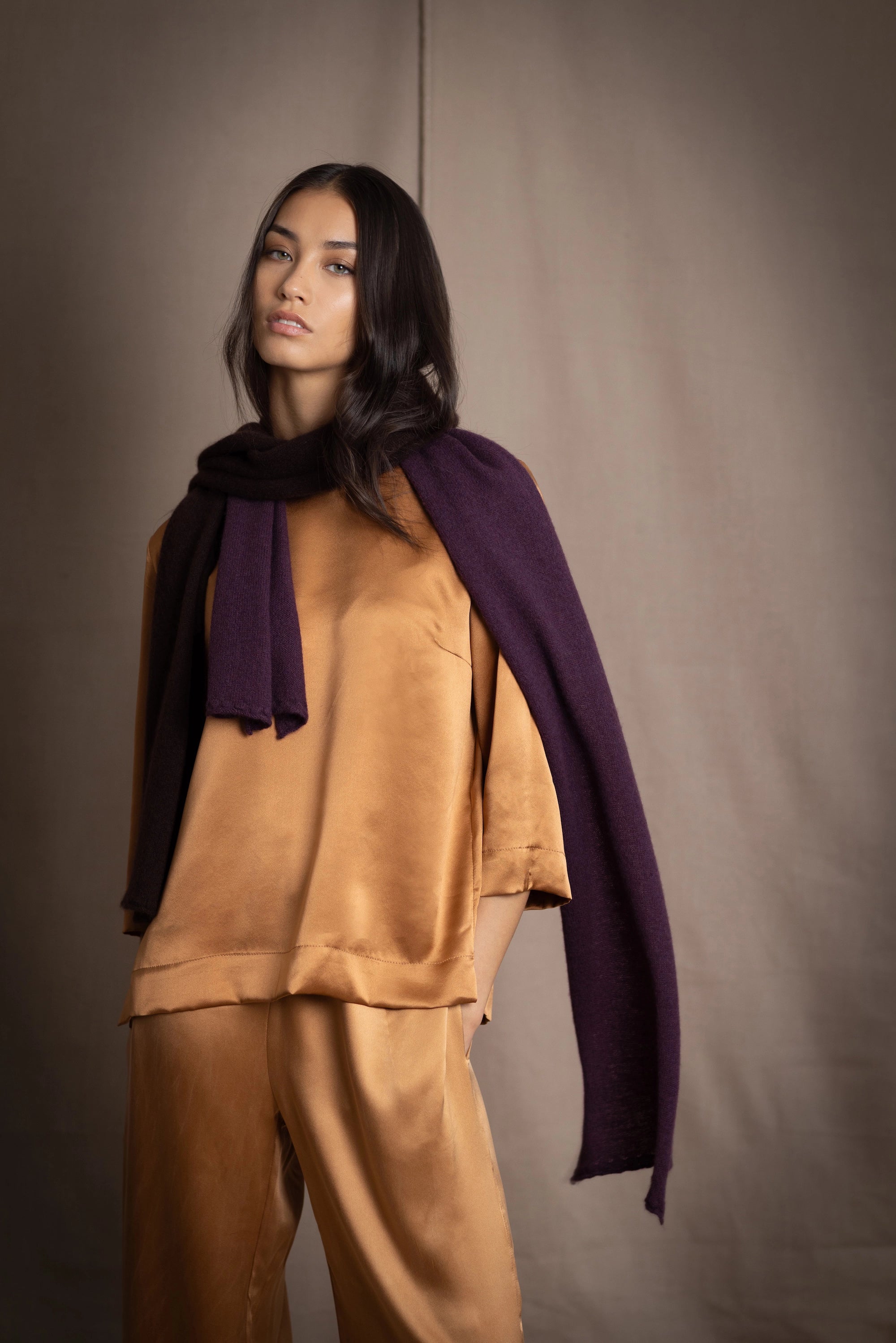 a woman wearing a cashmere scarf in dark purple over bronze silk clothing 