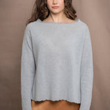 A woman wears a cashmere sweater jumper in pale turquoise blue with scallop trim detail along neck, sleeves and hemline