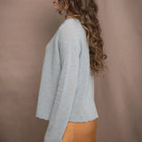 A woman wears a cashmere sweater jumper in pale turquoise blue with scallop trim detail along neck, sleeves and hemline