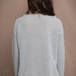 A woman wears a cashmere sweater jumper in pale turquoise blue with scallop trim detail along neck, sleeves and hemline
