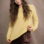A woman wears a cashmere sweater jumper in pale yellow with scallop trim detail along neck, sleeves and hemline with brown silk trousers