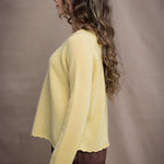 A woman wears a cashmere sweater jumper in pale yellow with scallop trim detail along neck, sleeves and hemline with brown silk trousers