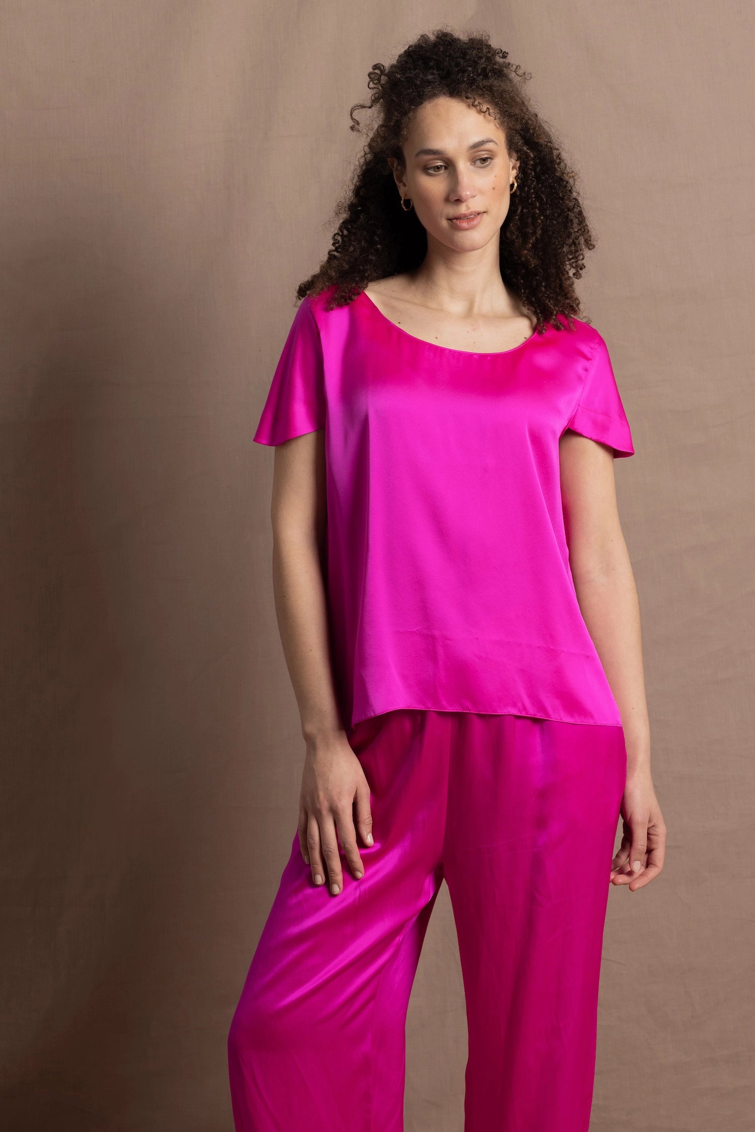 A woman wears a pure 100% silk t-shirt in bright pink with matching trousers