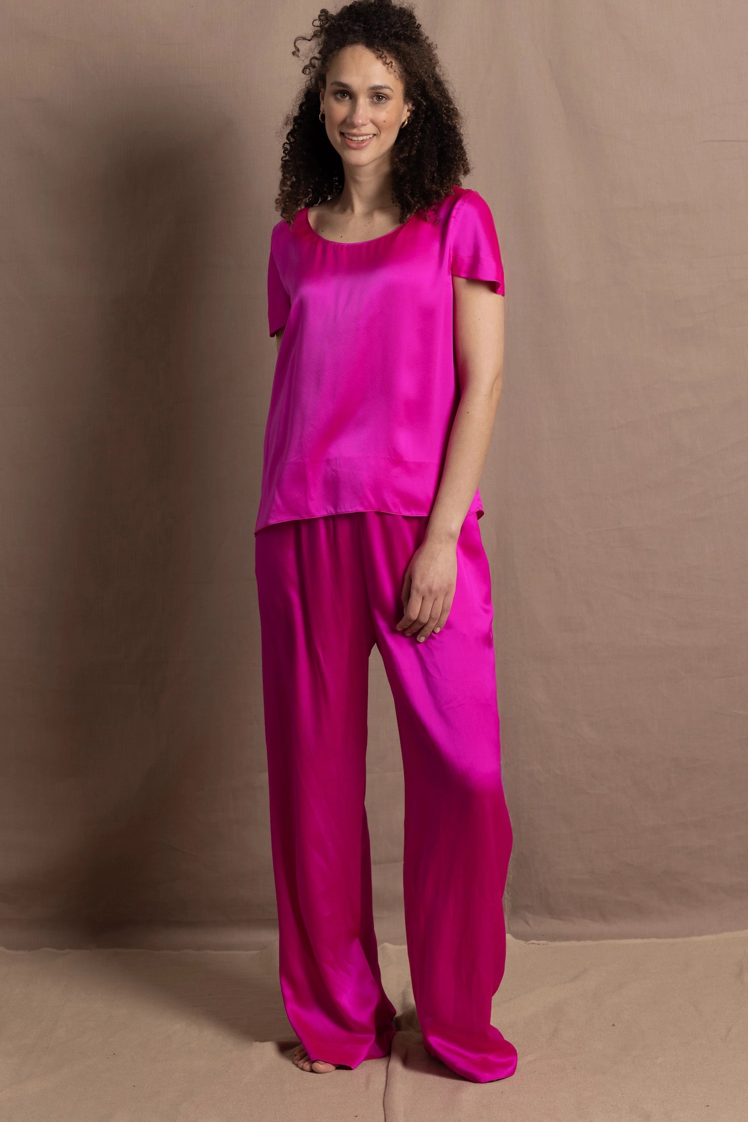 A woman wears a pure 100% silk t-shirt in bright pink with matching trousers
