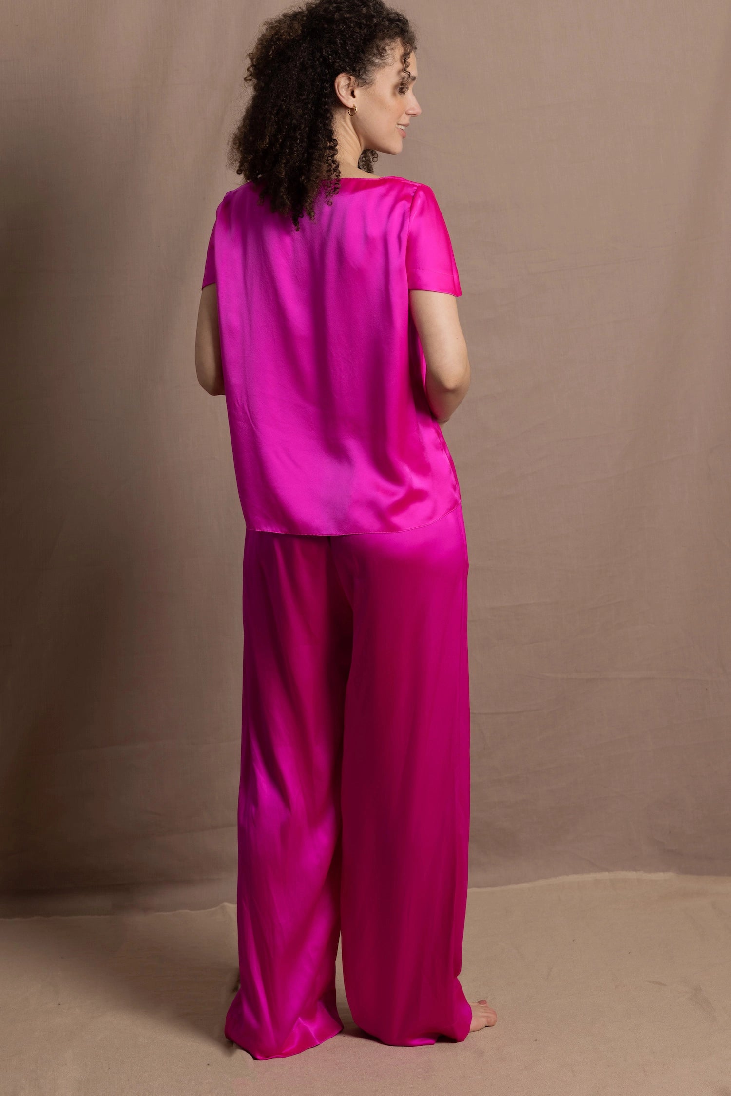 A woman wears a pure 100% silk t-shirt in bright pink with matching trousers