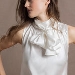 A  close up of a woman wearing  a 100% silk pussybow sleeveless blouse in white showing the bow