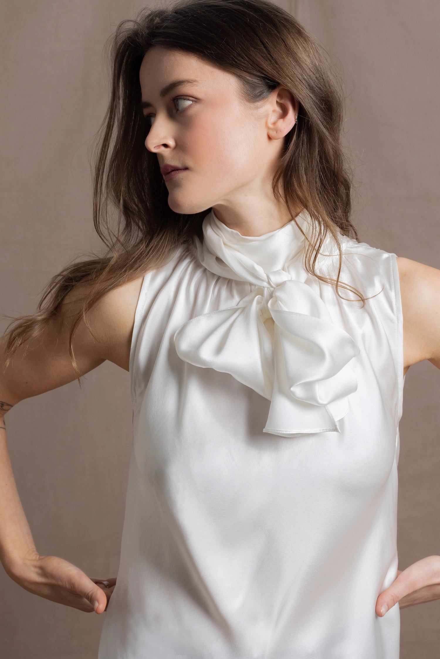 A  close up of a woman wearing  a 100% silk pussybow sleeveless blouse in white showing the bow