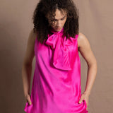 A woman wears a 100% silk pussy bow top in bright pink with matching trousers