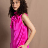 A woman wears a 100% silk pussy bow top in bright pink with matching trousers