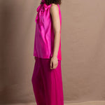 A woman wears a 100% silk pussy bow top in bright pink with matching trousers