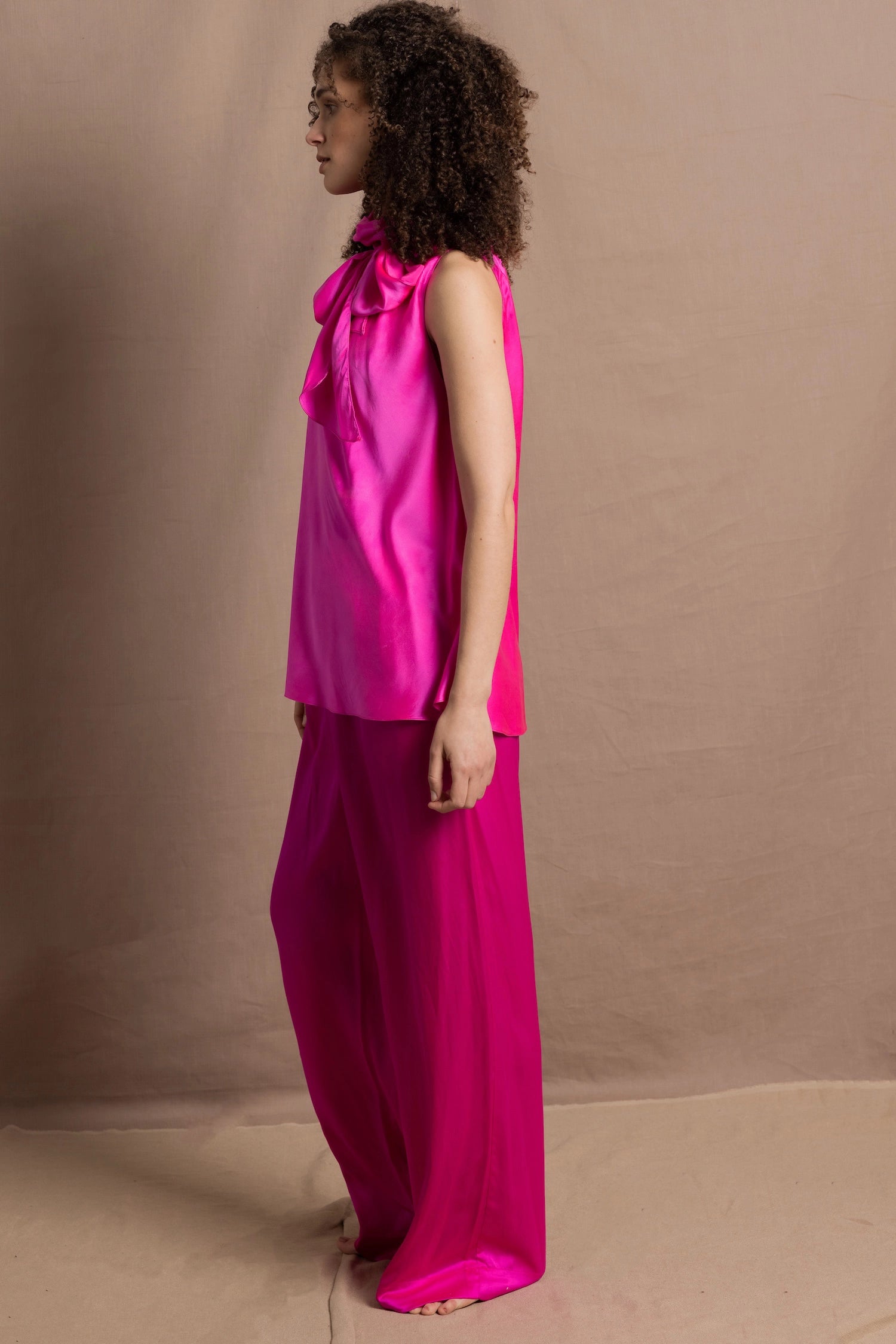 A woman wears a 100% silk pussy bow top in bright pink with matching trousers