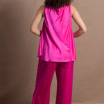 A woman wears a 100% silk pussy bow top in bright pink with matching trousers