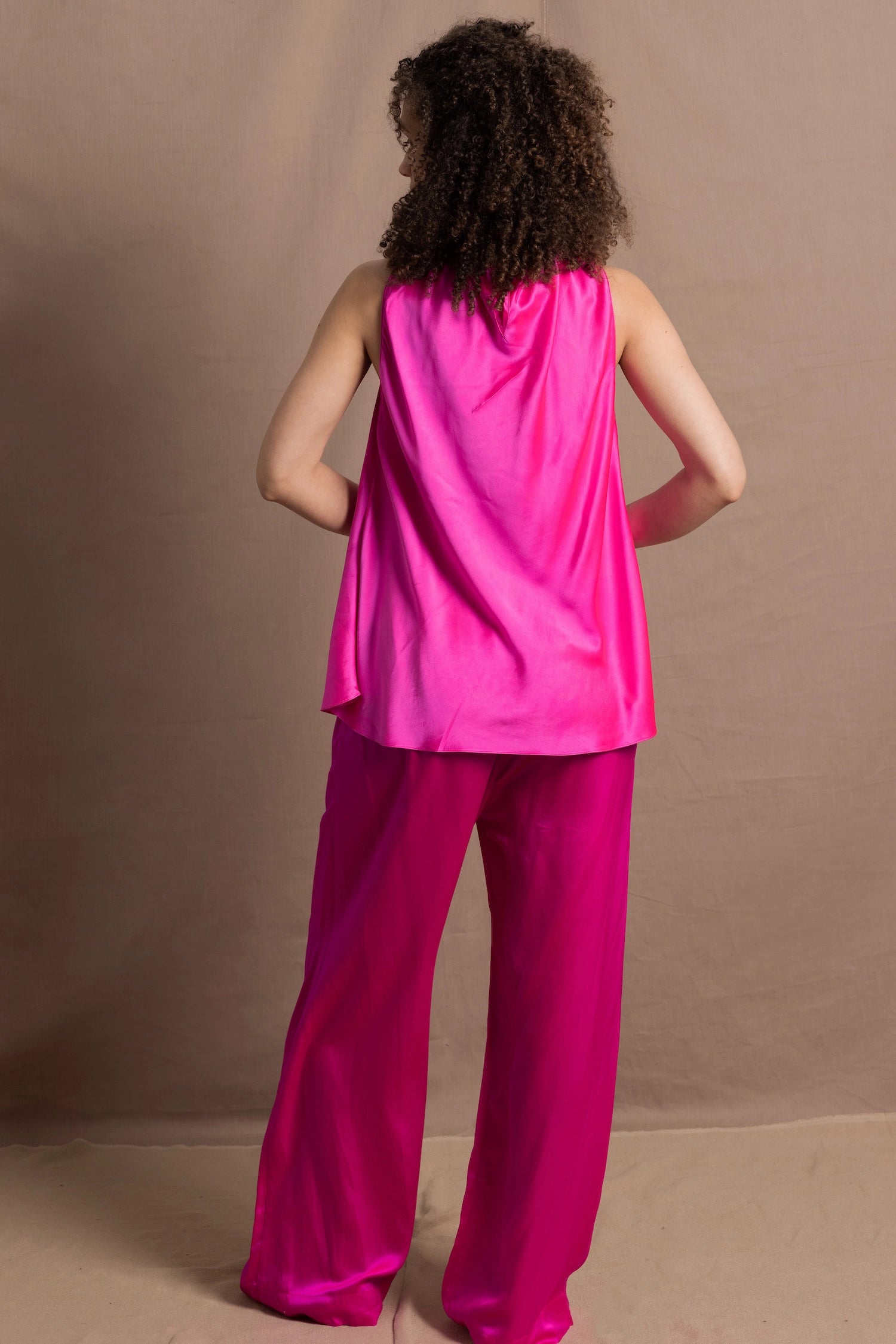 A woman wears a 100% silk pussy bow top in bright pink with matching trousers