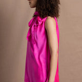 A woman wears a 100% silk pussy bow top in bright pink with matching trousers