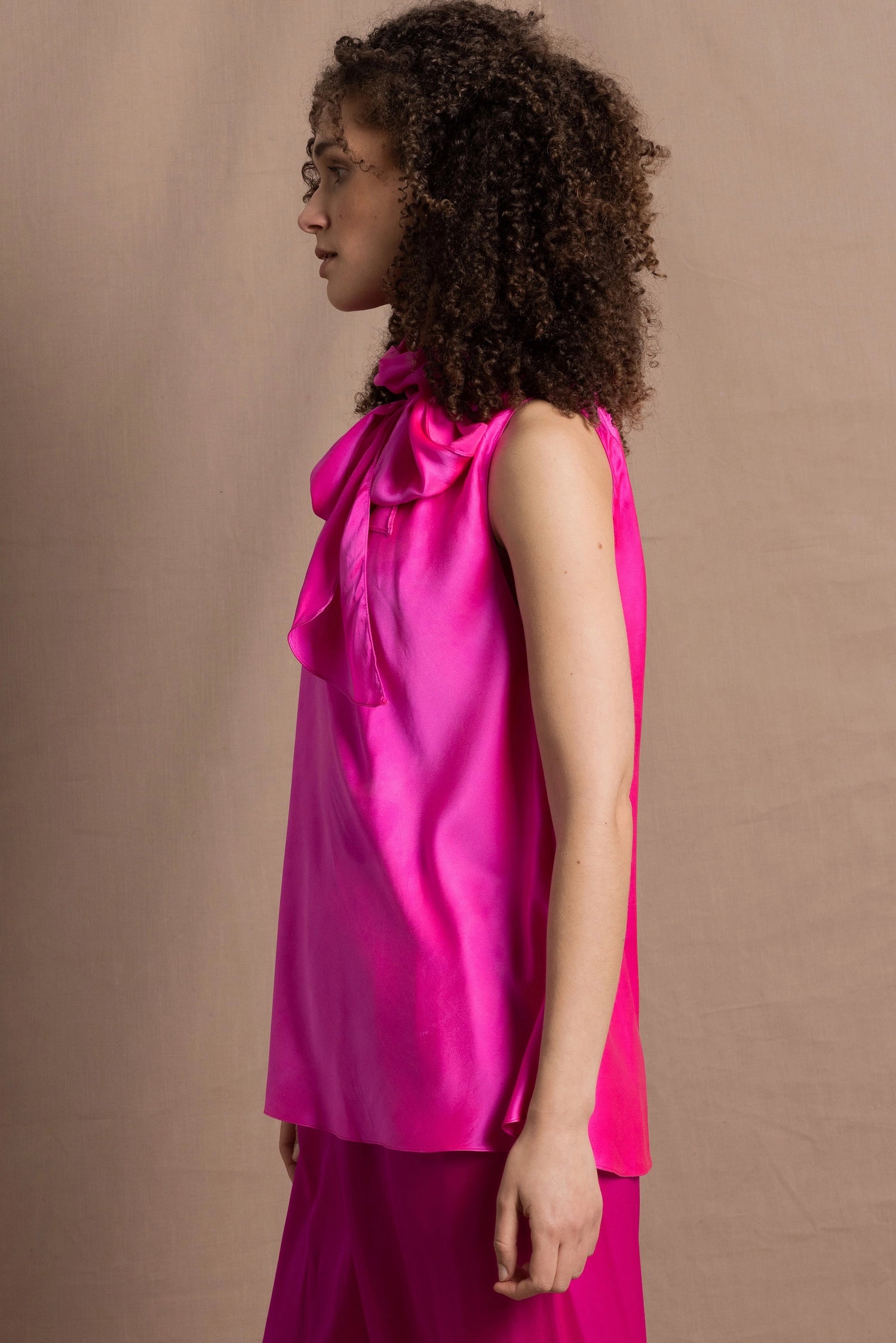 A woman wears a 100% silk pussy bow top in bright pink with matching trousers