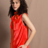 a woman wears a bright orange silk sleeveless top with bow around the neck and matching silk trousers