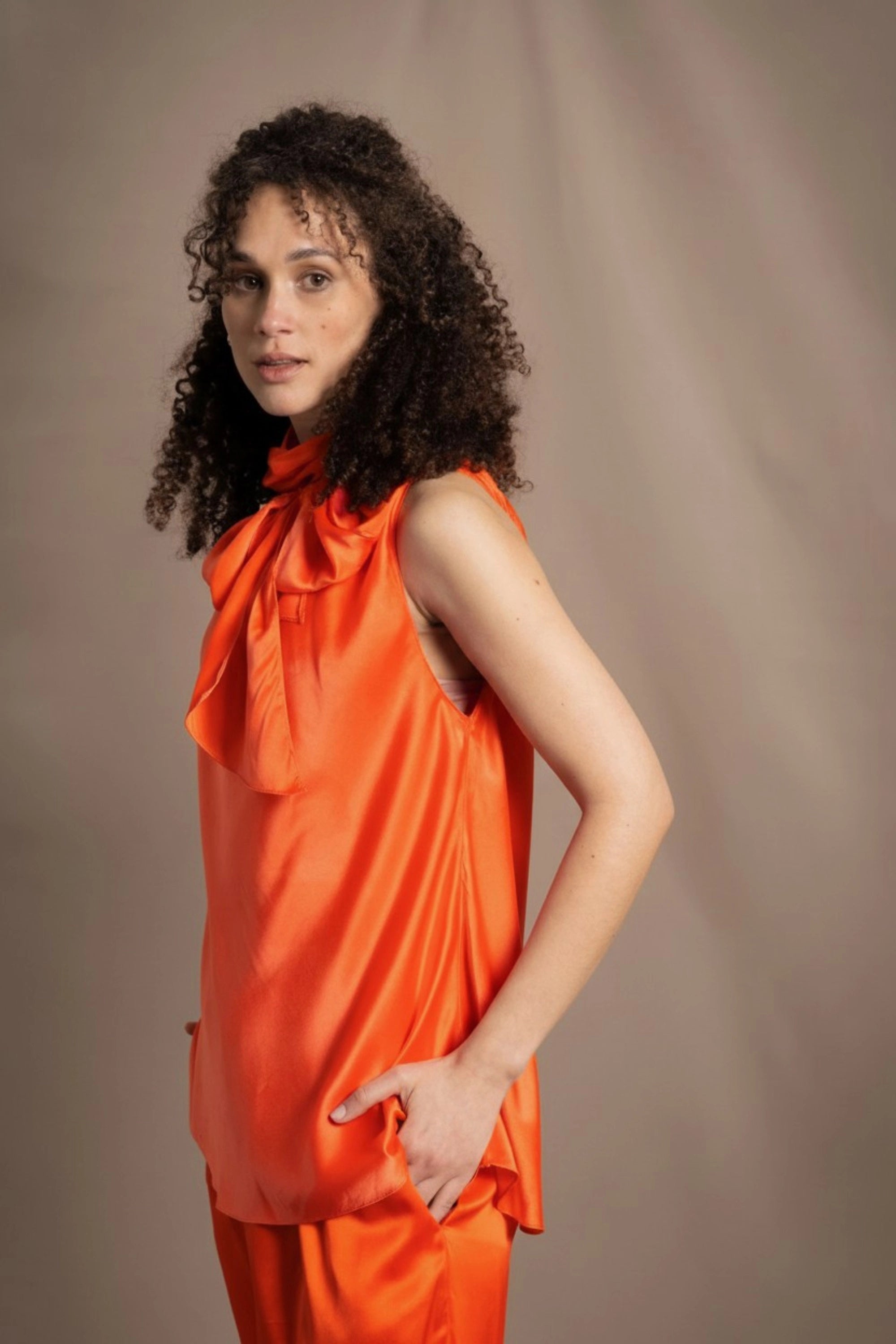 a woman wears a bright orange silk sleeveless top with bow around the neck and matching silk trousers