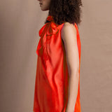 a woman wears a bright orange silk sleeveless top with bow around the neck and matching silk trousers
