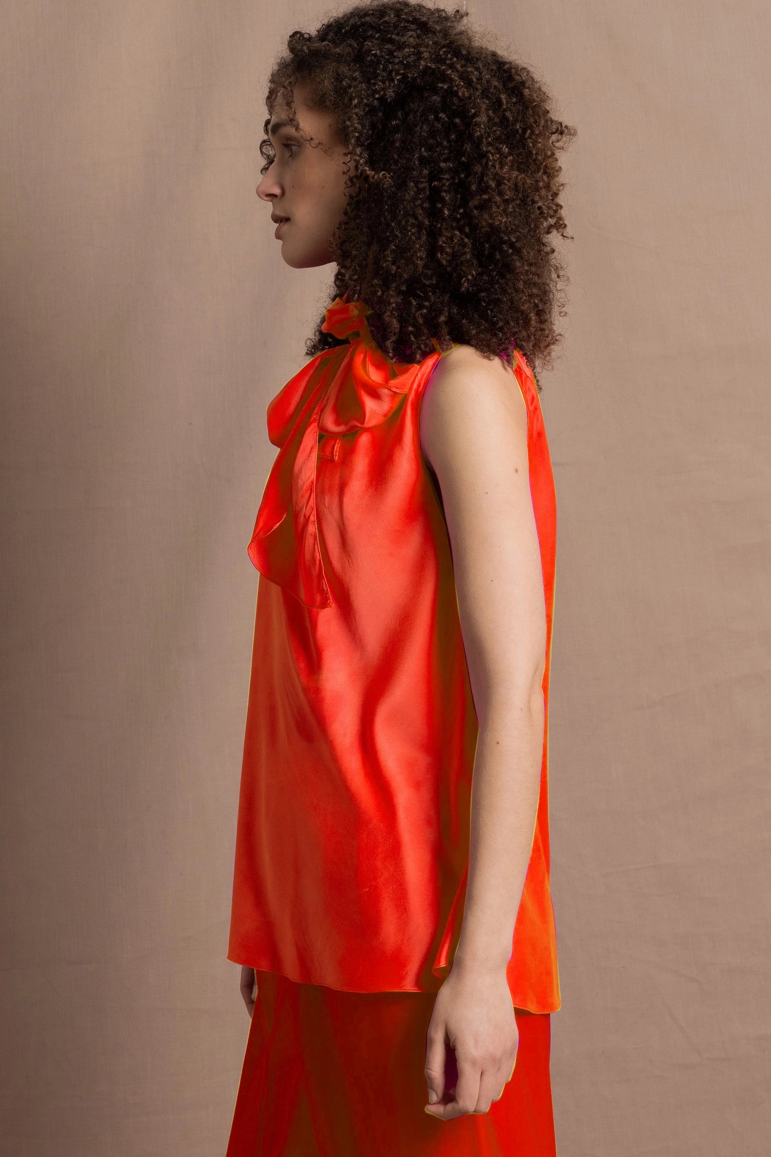 a woman wears a bright orange silk sleeveless top with bow around the neck and matching silk trousers