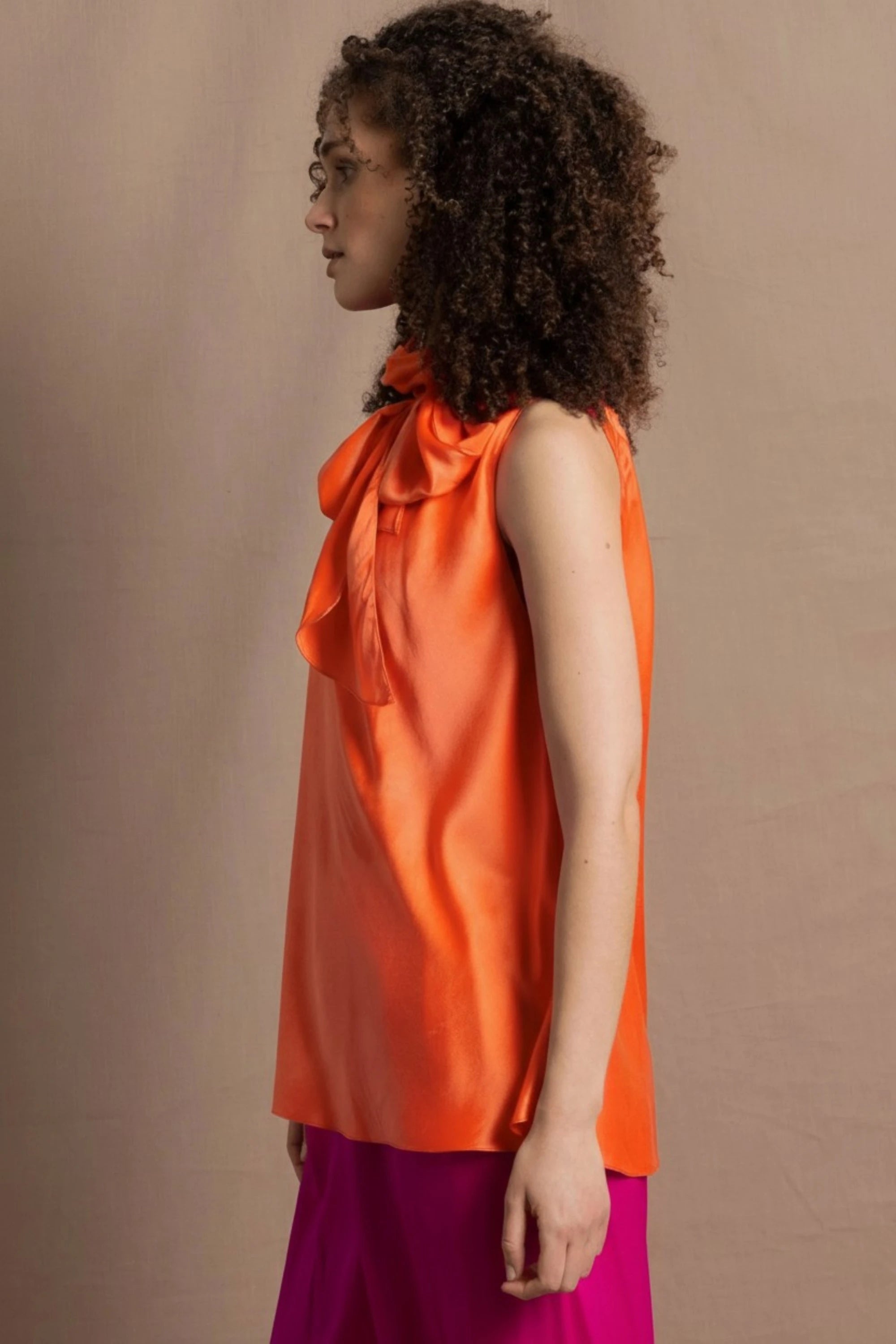 a woman wears a bright orange silk sleeveless top with bow around the neck and matching silk trousers