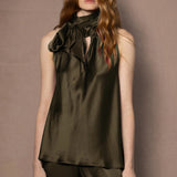 Woman wearing an olive green sleeveless silk top with a bow 