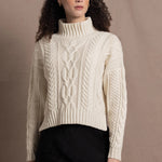 A woman wears a traditional Irish Aran Sweater made in 100% Cashmere over a black silk skirt