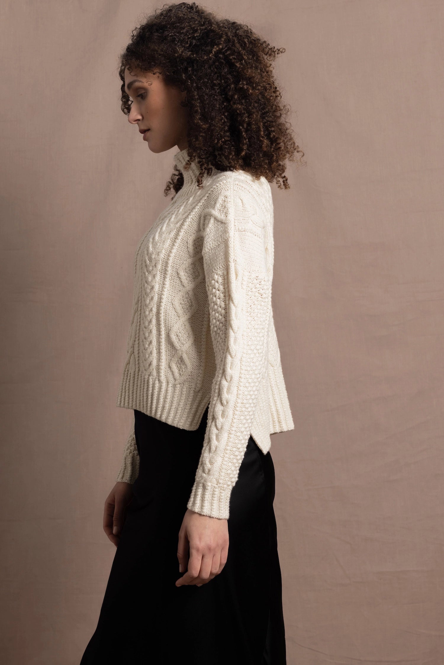 A woman wears a traditional Irish Aran Sweater made in 100% Cashmere over a black silk skirt